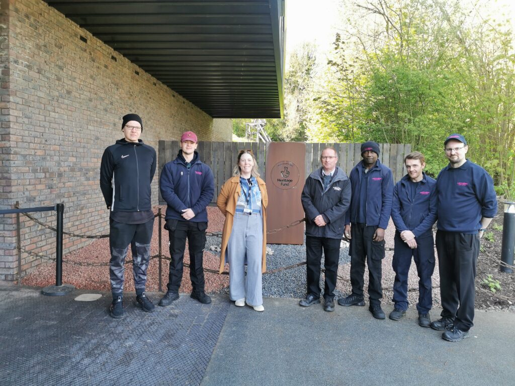 A photo showing the BCLM Lottery Funding Plate in situ after installation with the team involved in production